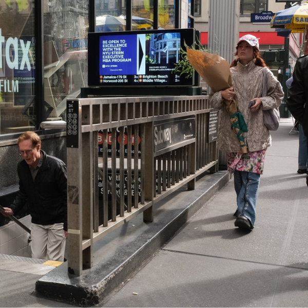 Woman walking by the subway entrance with NYU OOH ad behind her
